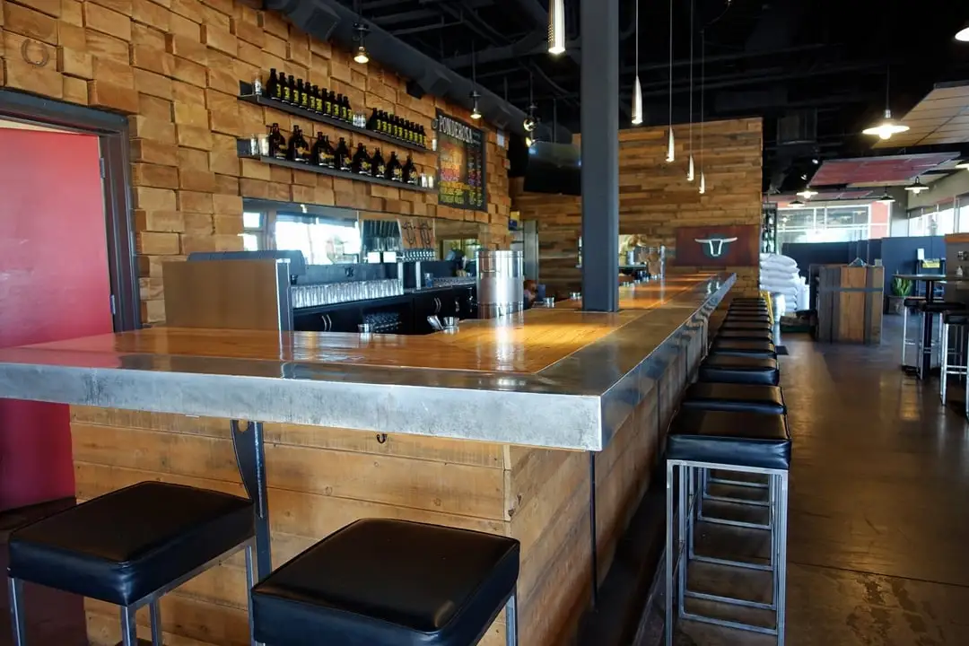 Long wooden bar with metal trim and cushioned stools.