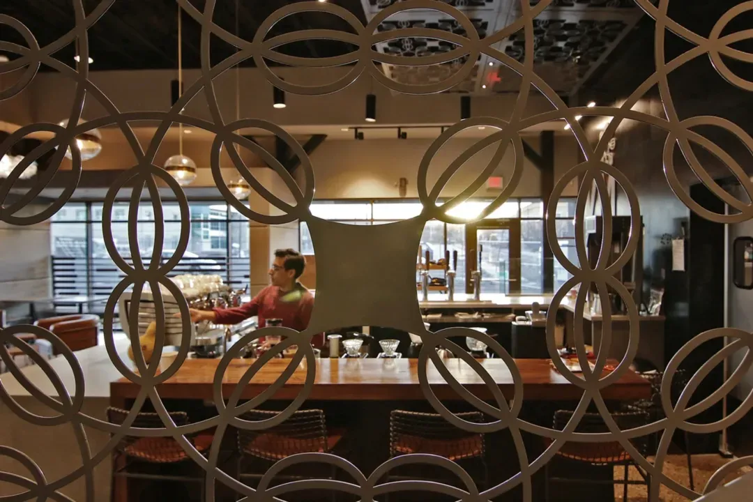 Abstract coffee bean metalwork next to coffee bar with barista working at the espresso machine.