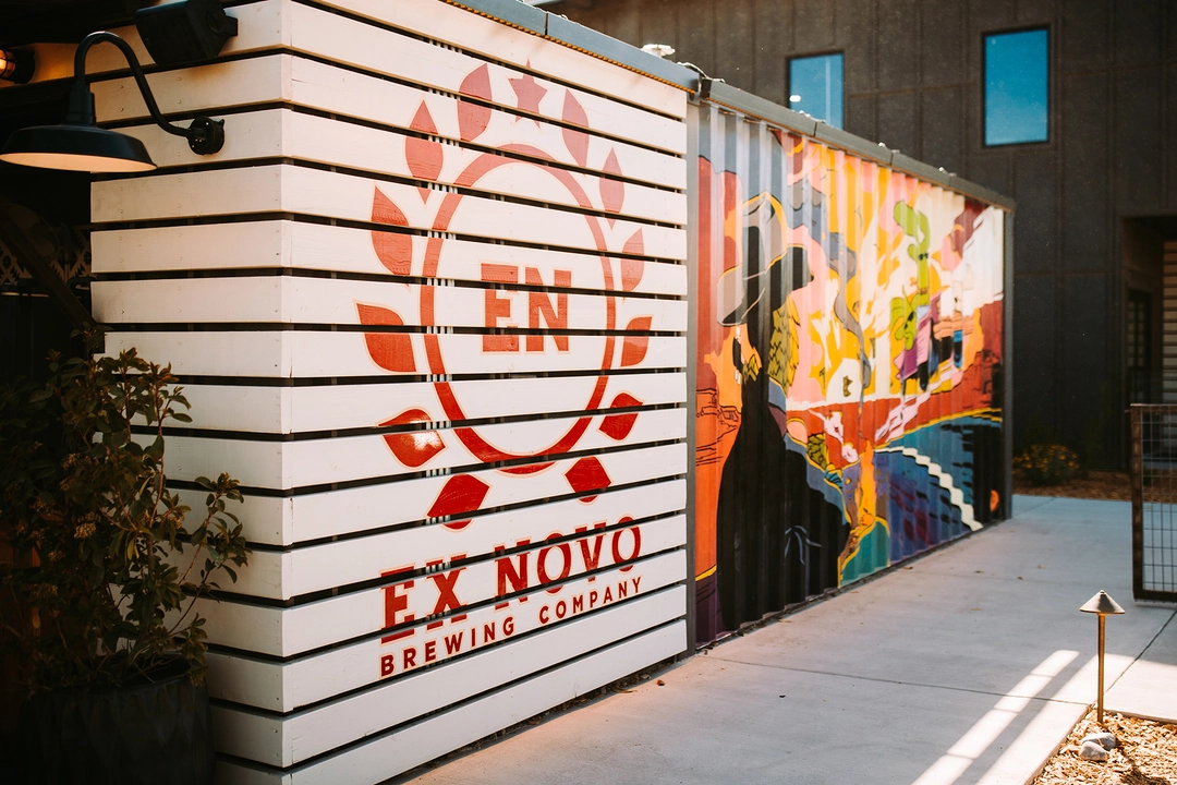 Storeage container building with Ex Novo branding and mural of cactus and hops characters in a comical southwestern scene.