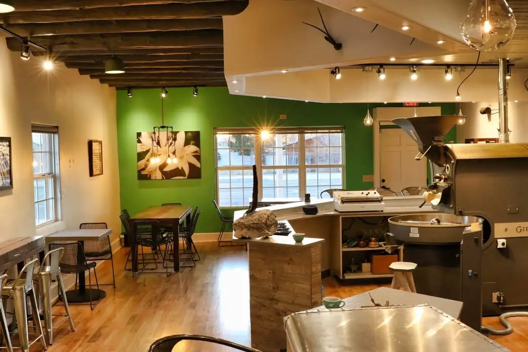 Cutbow Coffee Interior: Warmly lit tables and coffee bar with green wall and window looking out to the street.